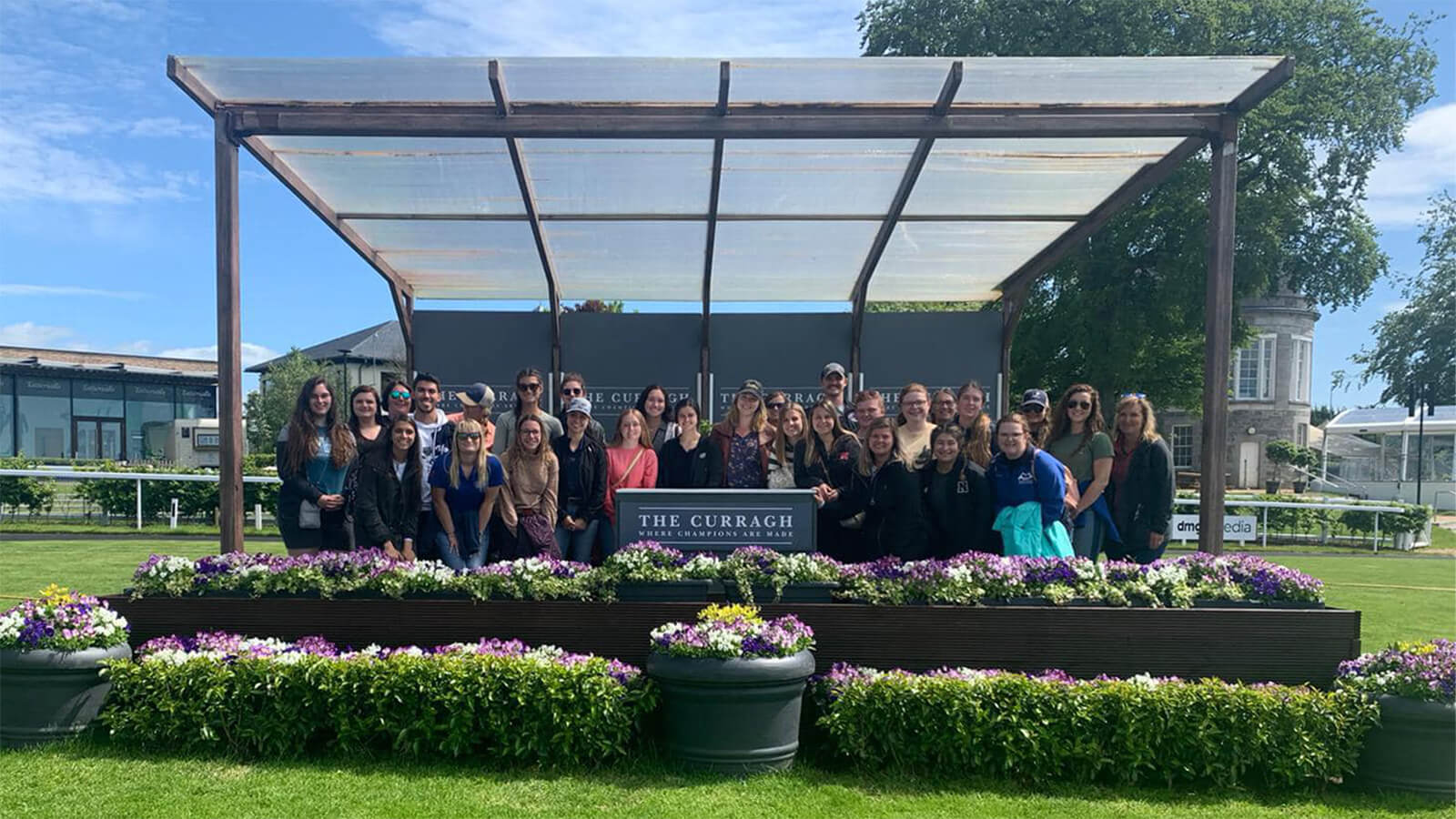 Students posing in front of a sign with the text "the curragh"