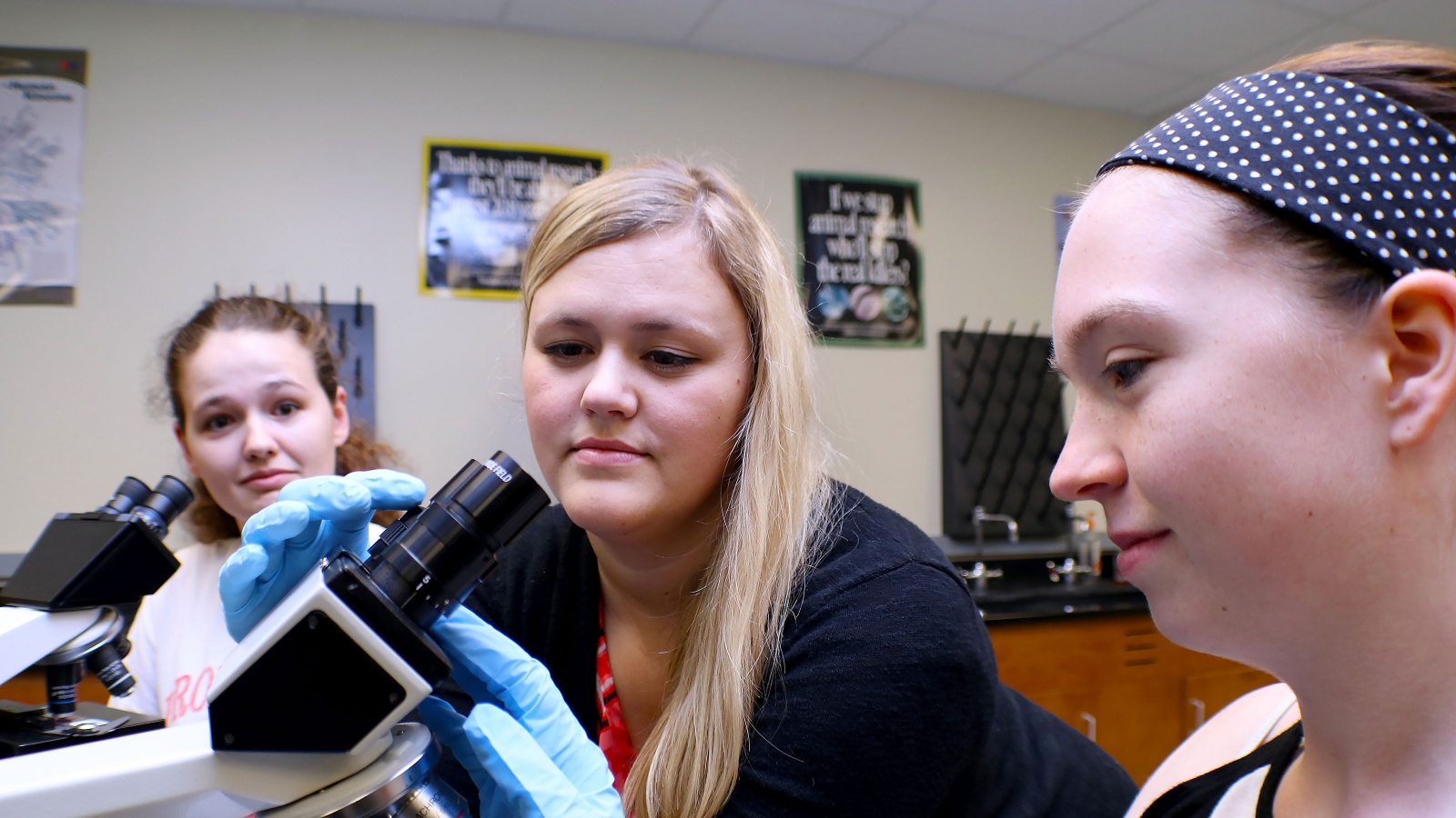 Two students looking through a microscope as another student looks on.